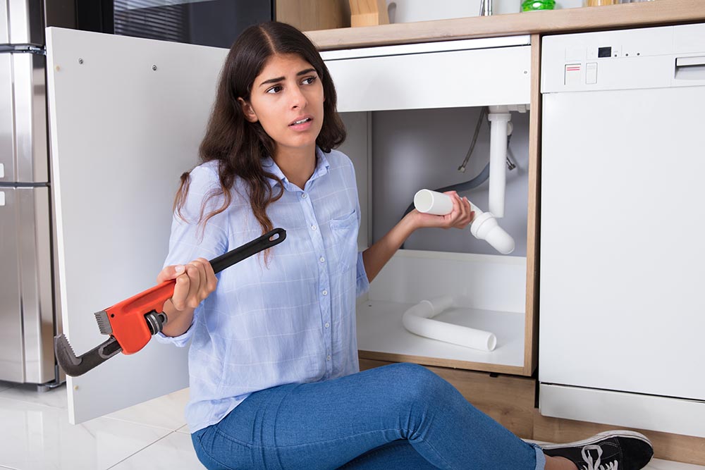 woman holding a wrench and attempting to fix a burst pipe